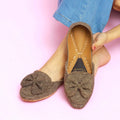 Brown flat Khussa shoes with a bow detail worn by a person on a pink background