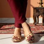 A lady wearing printed khussa shoes on a patterned rug with a warm-toned background