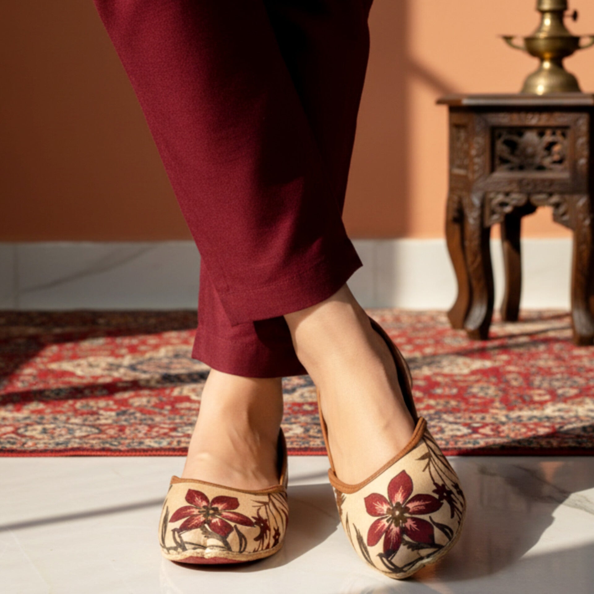 A lady wearing printed khussa shoes on a patterned rug with a warm-toned background