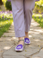 Woman wearing light purple pants and Purple Women khussa on a stone path with greenery.