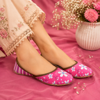 Pink flat khussa,shoes with a white and blue floral print and striped side panels, worn by a model in a pink-themed setting with a floral vase in the background.