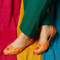 Orange embroidered flats worn with green pants on a colorful fabric background