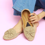 Beige flat khussa shoes with a bow detail worn by a person on a pink background