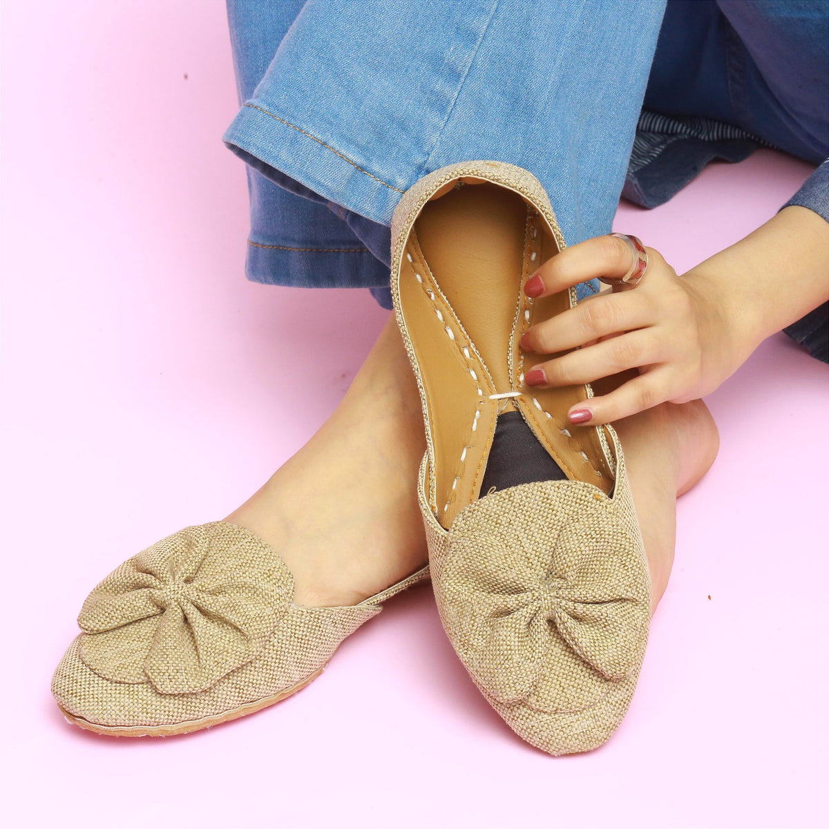 Beige flat khussa shoes with a bow detail worn by a person on a pink background