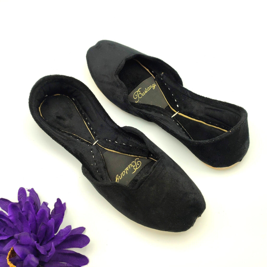 Pair of black ballet khussa with gold logo on a white background with a purple flower.
