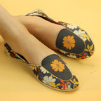 Floral patterned Khussa shoes worn by a female on a yellow background. 