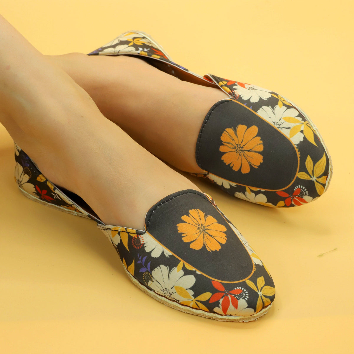 Floral patterned Khussa shoes worn by a female on a yellow background. 