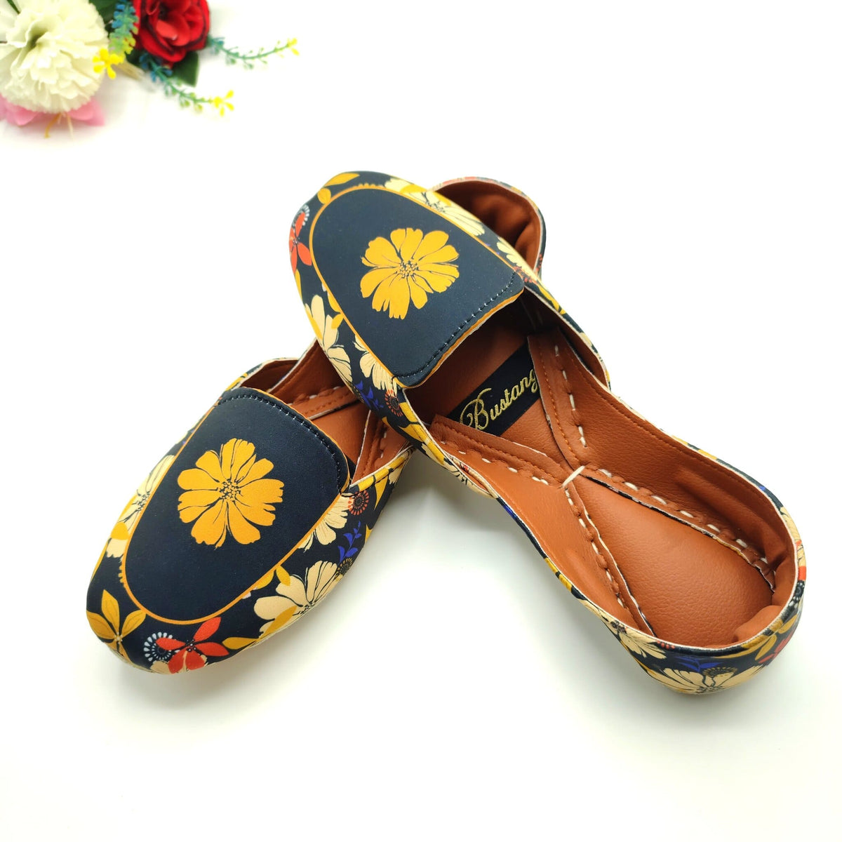 Floral patterned Khussa shoes worn by a female on a yellow background. 
