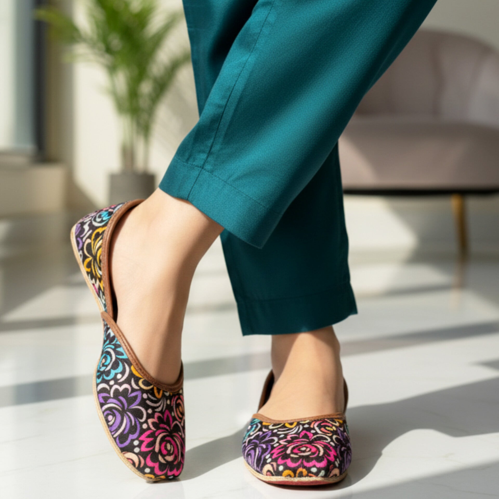 Colorful floral-patterned Printed Ladies khussa worn with teal pants on a light wooden floor.